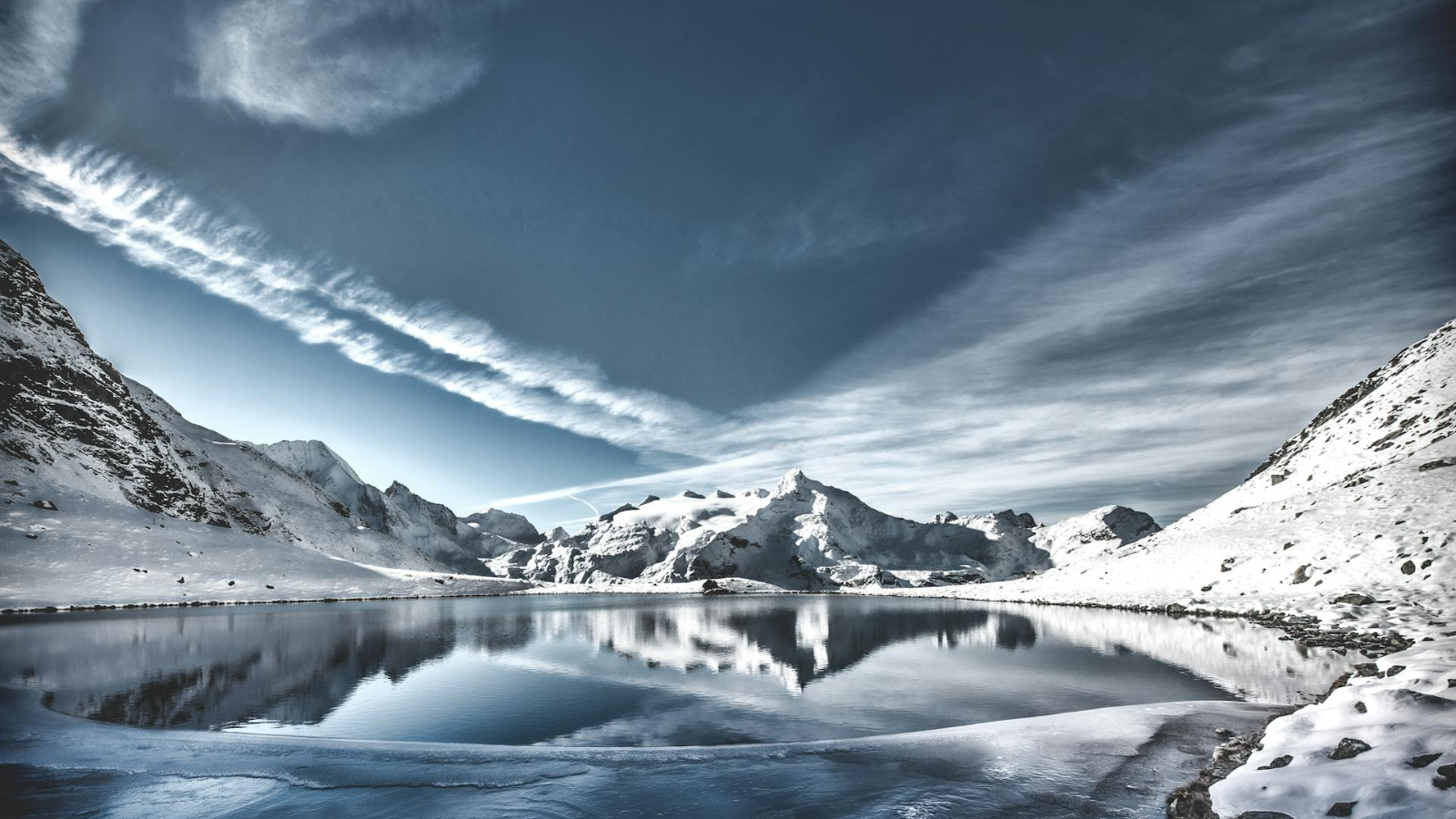 A lake surrounded by mountains with lots of snow. The skies are cloudy.